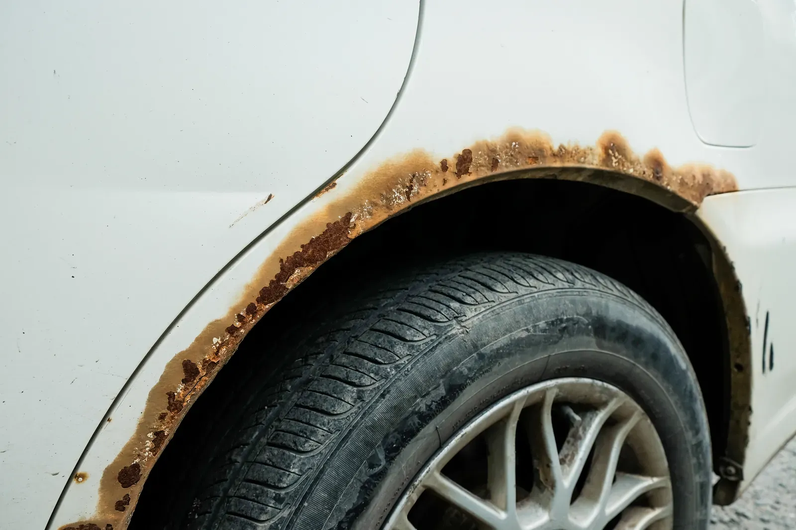 Early rust bubbles forming in the paint near a car’s wheel arch